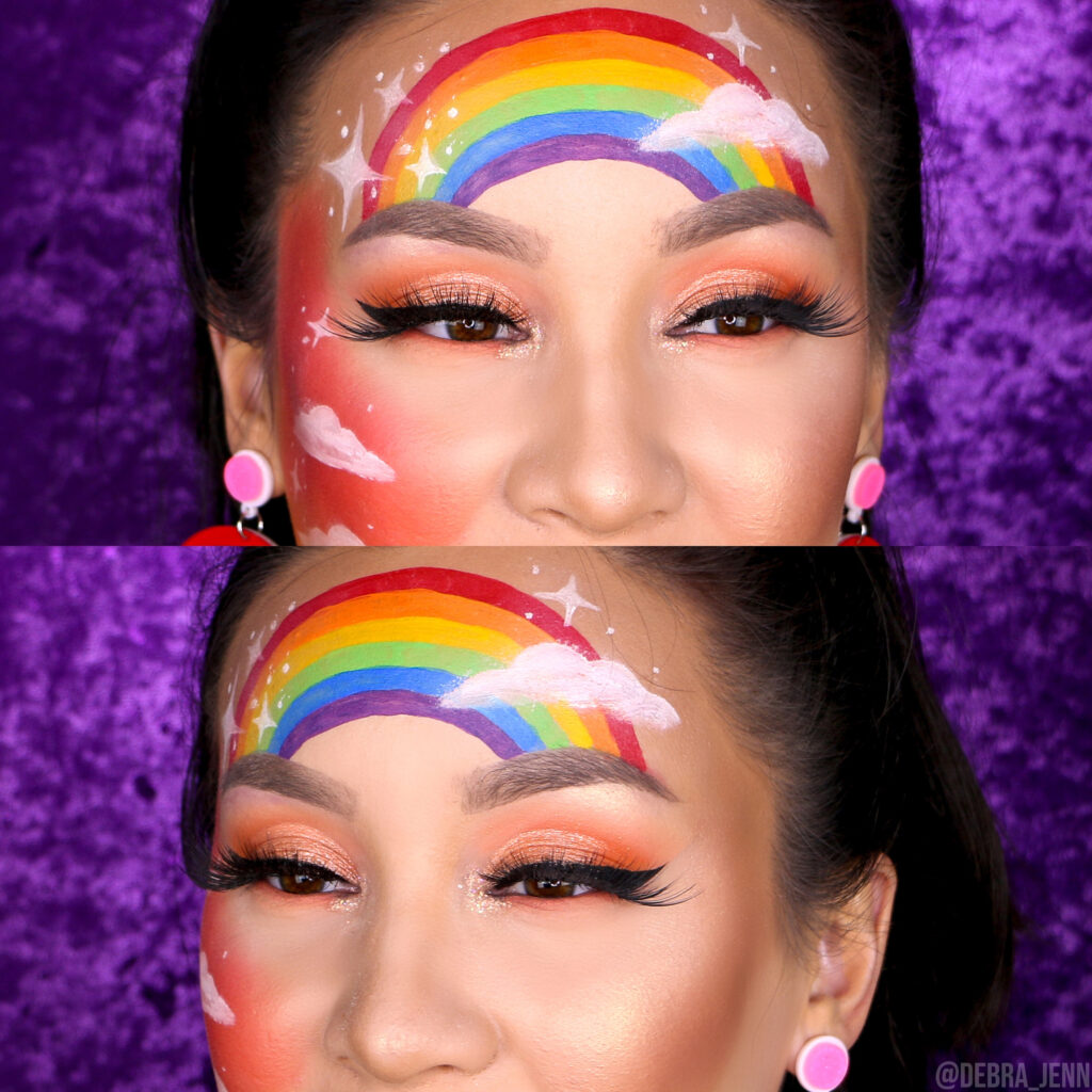 closeup of peach eyeshadow with rainbow cheeks and rainbow and clouds face painted on forehead and cheeks
