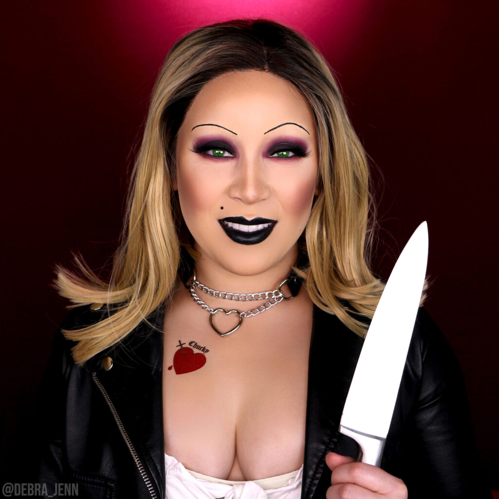 bride of chucky makeup with thin eyebrows, smokey eye, and black lips holding a knife