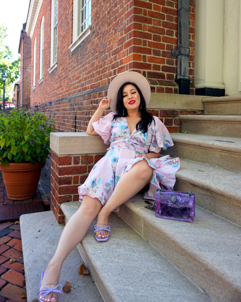 Debra Jenn wearing purple summer dress, clear purple purse, and hat, posed on stairs in colonial williamsburg