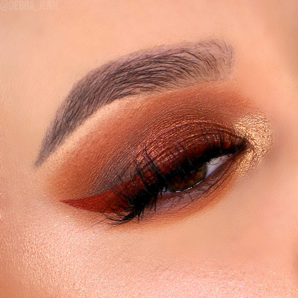 A closeup of Debra Jenn's eye showing a bronze orange eyeshadow look and red winged eyeliner