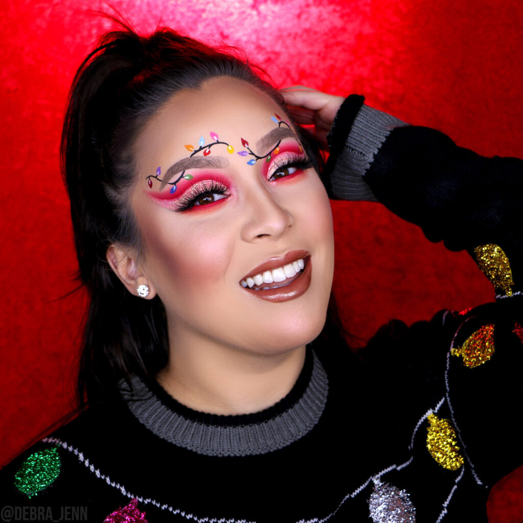 Debra Jenn in christmas lights eye makeup look with red eyeshadow and xmas lights drawn on eyebrows