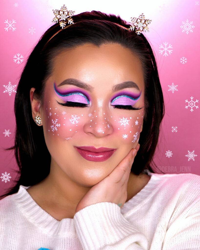 Debra Jenn in pink and purple eyeshadow with blue glitter eyeliner and snowflake makeup details on the cheeks