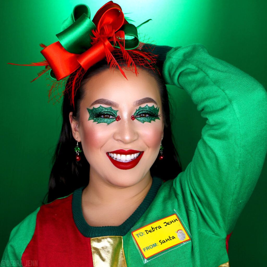 Debra Jenn in mistletoe makeup look with leaf shaped eyeshadow and red lips, wearing a christmas bow headband