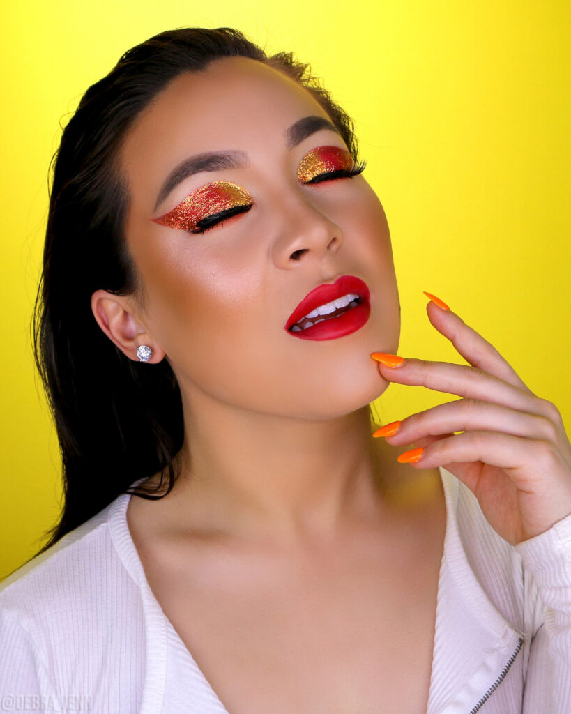 debra jenn wearing red and yellow glitter eyeshadow with red lips on a yellow backdrop